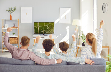 Excited family of four, mother, father and two children watching sport football match on tv...