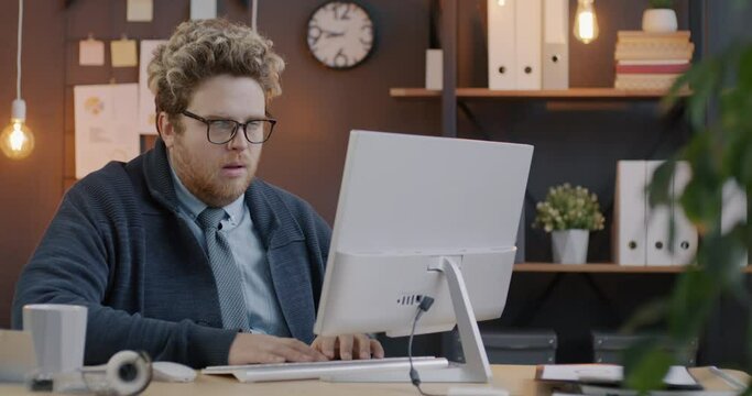 Loop of sleepy young employee using computer and falling asleep working overtime late in evening in modern office. Overwork and business concept.