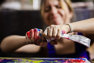 Close-up of a female artist squeezing multicolored paint from a tube onto a canvas, showcasing the...