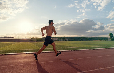 A man runs on a track with a cloudy sky in the background