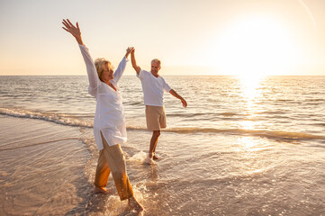 Happy Senior Old Retired Couple Walking Holding Hands on Beach at Sunset