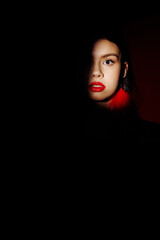 The face of a model girl in a spot of light on a black photo. Portrait of a model with bright makeup and red lipstick.