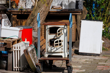 Obraz premium An old wood-burning stove with a hob stands among bulky waste on a trolley