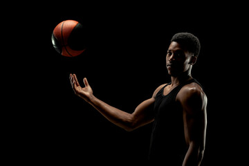 Basketball player holding a ball against black background. Serious concentrated african american...