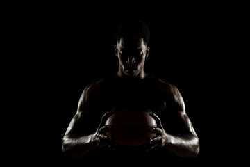 Basketball player holding a ball against black background. Serious concentrated african american...