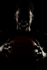 Basketball player holding a ball against black background. Distressed african american man...