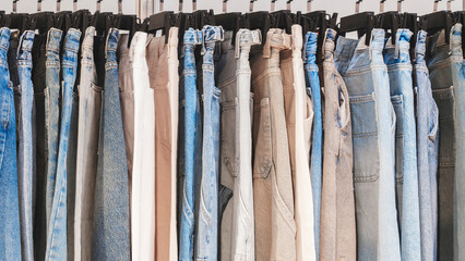 A row of jeans hanging on a rack, some are blue and some are white. The jeans are all different colors and styles
