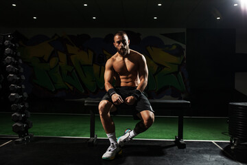 Focused male athlete sitting on bench in gym with graffiti background, showcasing strength and determination