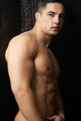 Fototapeta premium Cleaning, portrait and man in shower for muscle, body hygiene and wellness for skin routine in studio. Grooming, skincare and male model with wash, water and self care confidence on black background