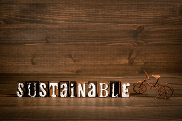 SUSTAINABLE word from alphabet blocks and rusty miniature bicycle on wood texture background