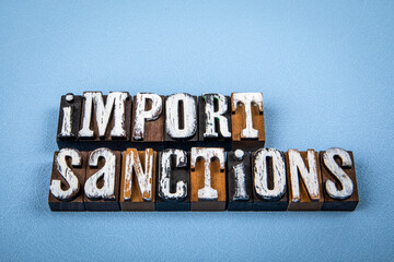 IMPORT SANCTIONS. Wooden alphabet letter blocks on blue textured background