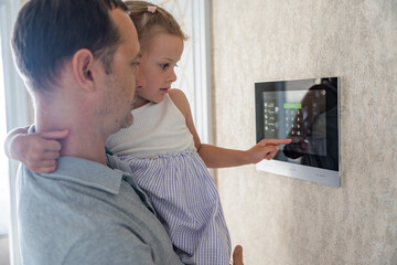 Daughter in her father using tablet panel application for control smart home living. Wireless device controller for home automation IoT on the wall