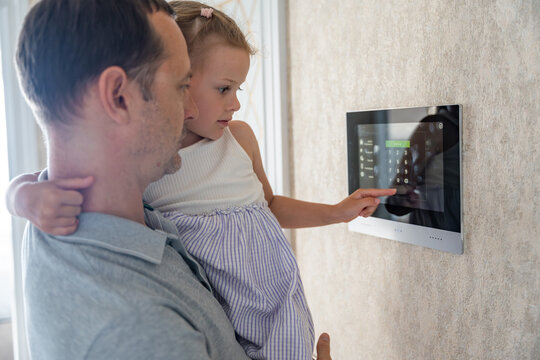 Daughter in her father using tablet panel application for control smart home living. Wireless device controller for home automation IoT on the wall