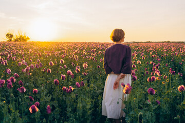 young woman carries a bouquet of poppies in her hand at sunset