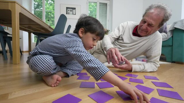 Grandfather lying on the floor and playing a matching game with his young grandson, both in pajamas, enjoying a playful and engaging moment, family interaction, intergenerational bonding at home