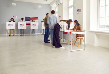 Fototapeta premium Side view portrait of young girl american citizen registering at polling station with American flags on election day. USA voters standing in queue at vote center and putting ballots in voting booth.
