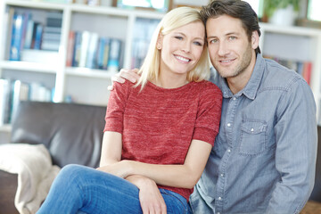Obraz premium Couple, portrait and hug on sofa in home living room, bonding or relaxing and having fun. Smile, man and woman sitting on couch for embrace, happiness and enjoying security together for support