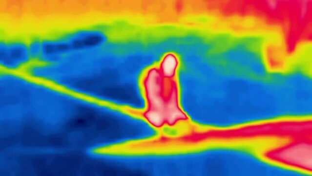 A tourist forces a river over a thrown log.Image from thermal imager device.