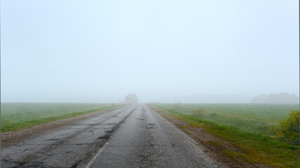 Broken asphalt road on an early foggy morning. Road in need of repair.