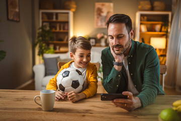 Father and son watch football match on mobile phone and cheer at home