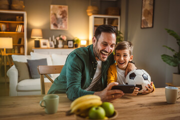 Father and son watch football match on mobile phone and cheer at home