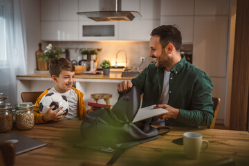 Dad help his son to pack his notebook and book for school in backpack