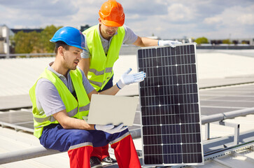 Repairmen on the roof, using a laptop to adjust, repair, or maintain solar panels. Work ensures the...