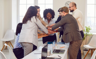Group of business people standing in a circle in an office, stacking hands together. Gesture...