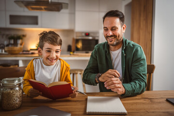 Son read a book and have fun while spend time with his father at home