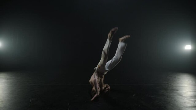 Group of a professional dancers are practicing capoeira in darkness against a spotlight on a black background of studio. Afro-Brazilian martial art that combine elements of dance.