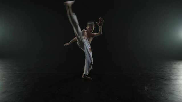 Group of a professional dancers are practicing capoeira in darkness against a spotlight on a black background of studio. Afro-Brazilian martial art that combine elements of dance.