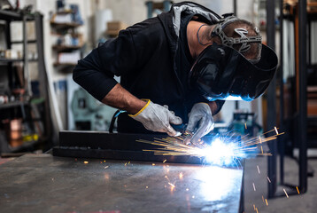 Performing a weld: the man in the welding mask is positioned with the welding machine on the...