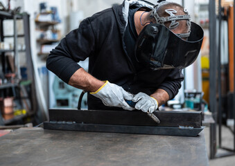 Performing a weld: the man in the welding mask is positioned with the welding machine on the welding point. Copy space.