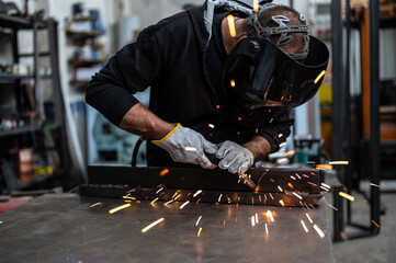 Performing a weld: the man in the welding mask is positioned with the welding machine on the...