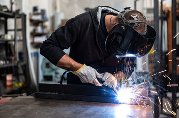 Performing a weld: the man in the welding mask is positioned with the welding machine on the...