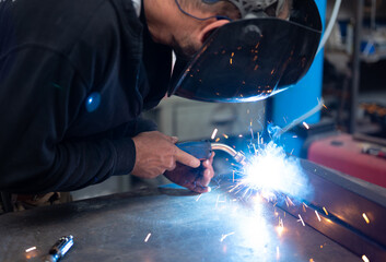 Spectacular conceptual image of a blacksmith busy using the welding machine. Sparks and smoke flash...