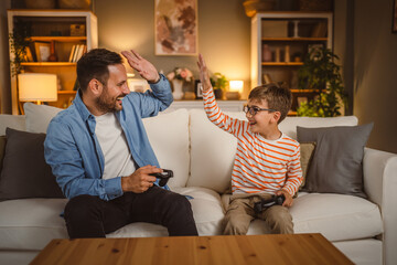 Adult caucasian father and son play video games with joystick at home