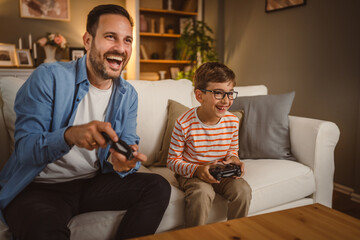 Adult caucasian father and son play video games with joystick at home