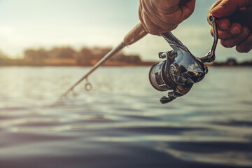 Freshwater fishing in summer. Spinning reel on a spinning rod in the hands of a fisherman.