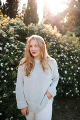 Portrait of beautiful blonde woman 22-24 year old wearing knitted sweater over flowers outdoor. Looking at camera. Spring time.