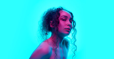 Portrait of beautiful young woman with curly hair, nude makeup look posing against cyan background...