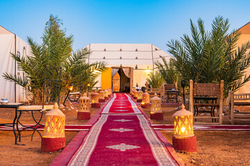 Luxury tent camp illuminated with fire lamps at Erg Chebbi Sahara desert at evening near Merzouga...