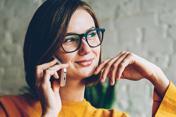 Pondering business woman in eyeglasses listening funny story from friend during mobile conversation...