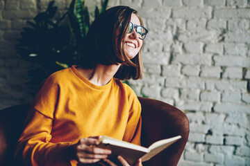 Positive young woman dressed in casual yellow sweater with mock up area laughing during reading...