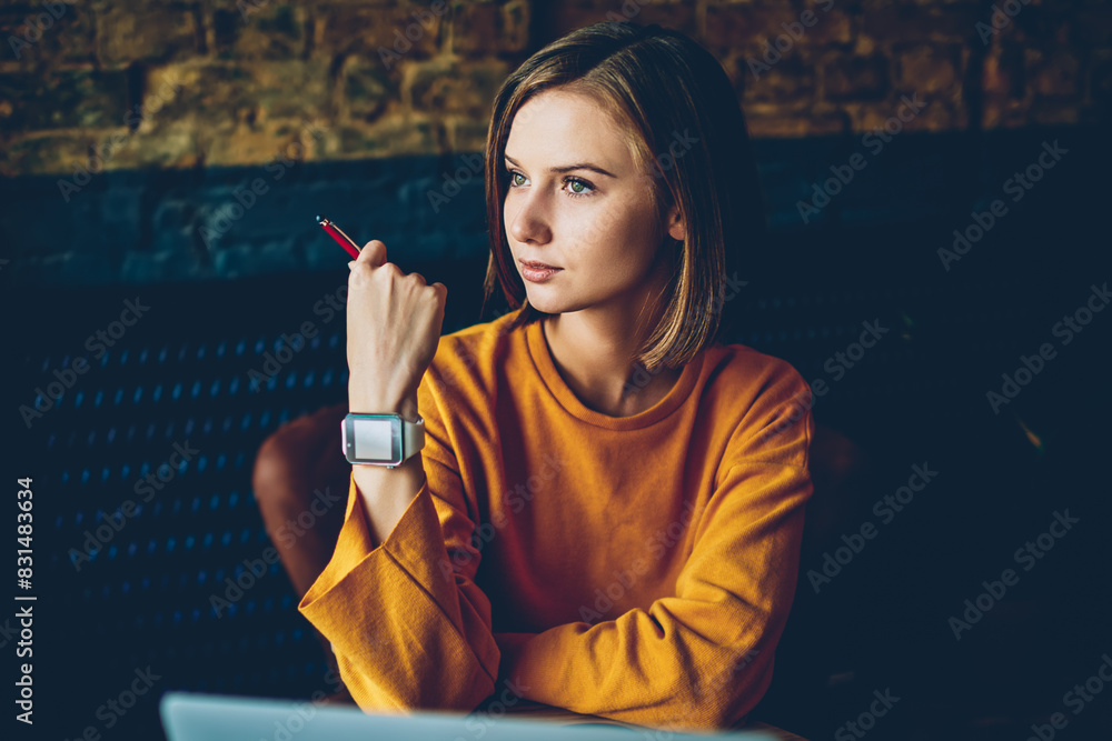 Poster charming thoughtful hipster girl with modern smartwatch on hand looking out of window and thinking o