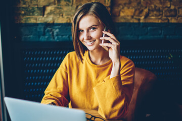 Half length portrait of cheerful female manager talking with client on digital telephone working...