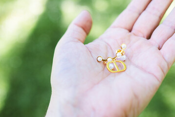 A young woman displays a gold and pearl earring in the palm of her hand in a natural outdoor setting