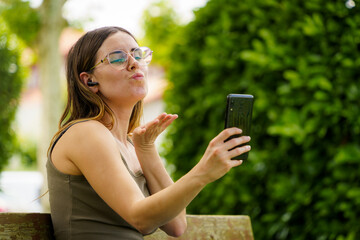 Young Caucasian Girl Making a Video Call with Her Phone. Blowing a Kiss with Her Mouth and Hand...
