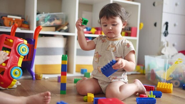baby plays with blocks on the floor in kindergarten. happy family kid concept. baby girl builds a tower from cubes and plays with toys. development of fine motor lifestyle skills concept