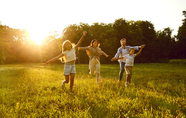 Happy family running and having fun in summer park enjoying sunny day in nature. Mother, father and...